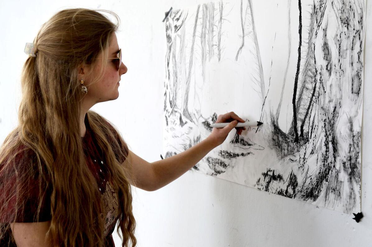 A female Art Club member creates art on a wall during an Art Club meeting
